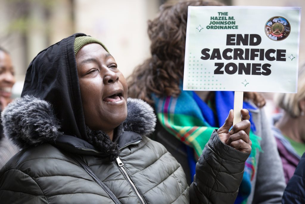 A woman in a winter coat holds a sign that says "End Sacrifice Zones."