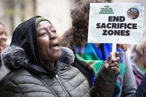 A woman in a winter coat holds a sign that says "End Sacrifice Zones."