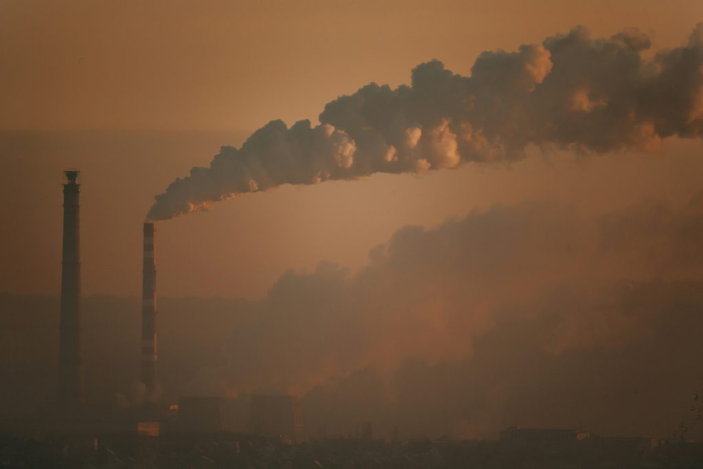 Smoke stacks with white plumes of smoke in an orange sky.