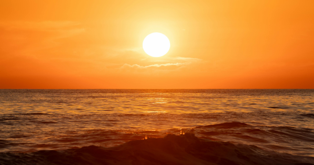 Orange sun over water at a beach.