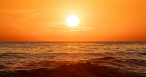 Orange sun over water at a beach.