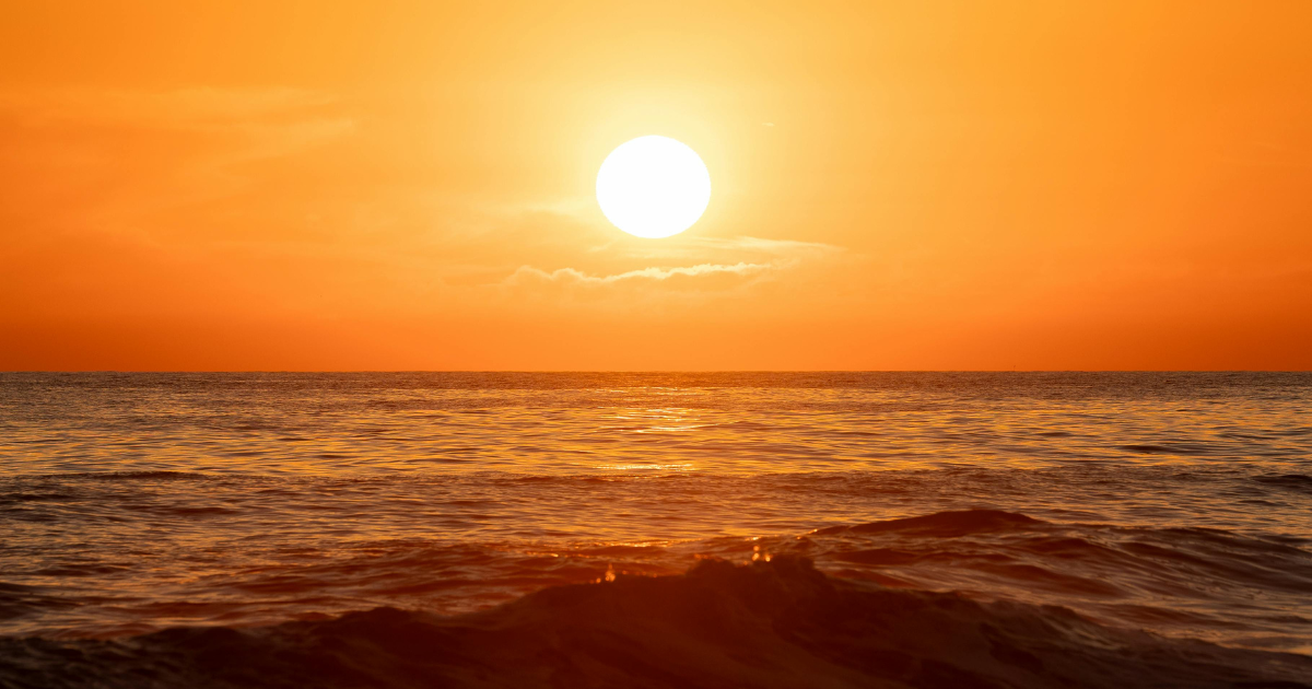 Orange sun over water at a beach.